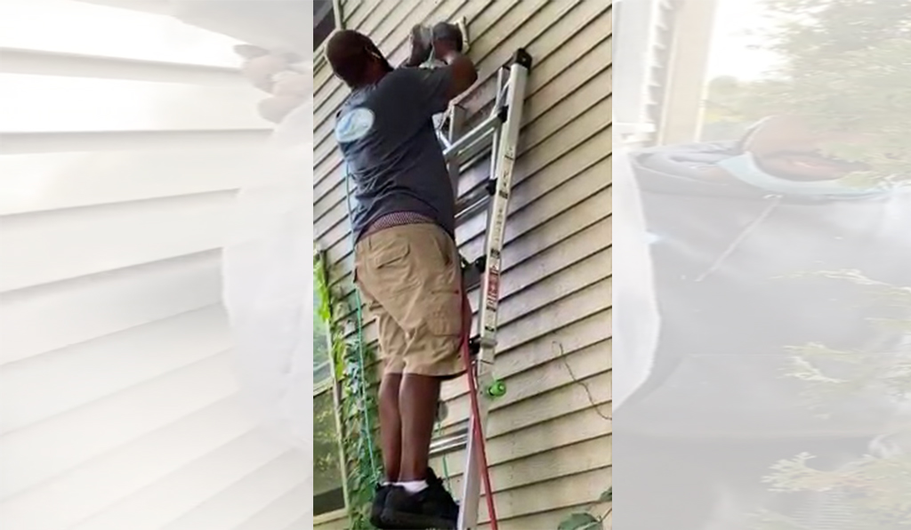 Owner of Totally Clean standing on a ladder reaching a high dryer vent on the exterior of the home.