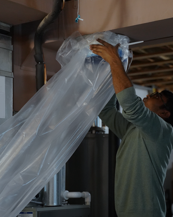 Technician hooking up equipment to furnace to seal ducts.